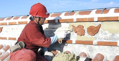 首里城正殿の屋根に登り、しっくいを塗る田端忠さん＝2010年10月、那覇市（本人提供）