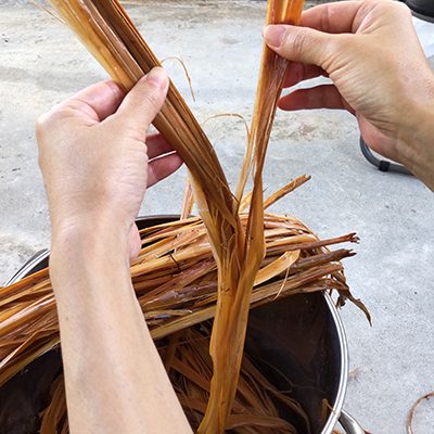（2）たたいた茎を大鍋で2時間ほど水から煮る。柔らかくなった茎の皮を一枚ずつ剥がす。