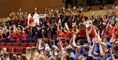 開会式で出場国が紹介され、立ち上がって手を振る日本代表の選手たち（奥）＝20日、糸満市のシャボン玉石けんくくる糸満（小川昌宏撮影）