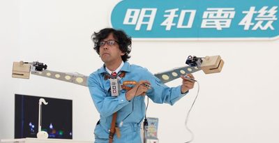 内覧会で指パッチン式電動木魚「パチモク」を演奏する明和電機の土佐信道社長＝7月12日、那覇市の県立博物館・美術館（大城直也撮影）