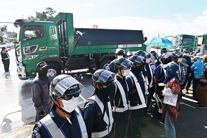 土砂搬出再開に抗議する市民らを機動隊が排除後、土砂を積んで国道に出るダンプ＝22日、名護市安和（ジャン松元撮影）