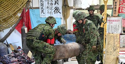 ヌチドゥタカラの家に展示された模擬爆弾とみられるものを運ぶ陸上自衛隊員ら＝4日、伊江村